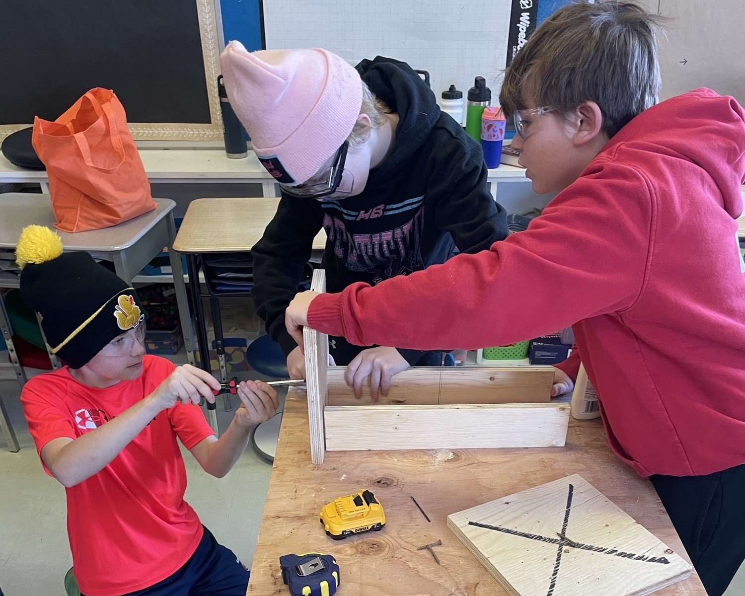 Three students working together to build lap desk. Two students holding the wood, and one student using a screwdriver