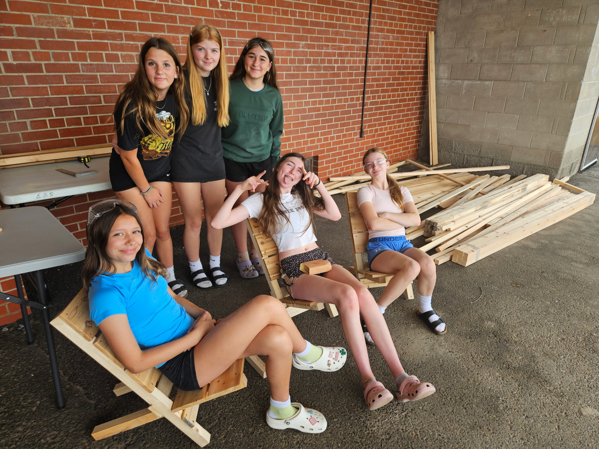 A group of students stand outside showing the folding chairs they built