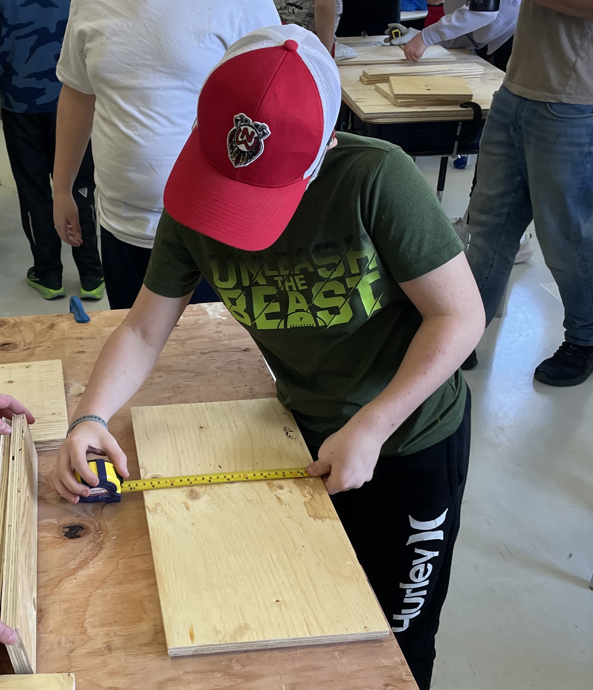 One student using measuring tape to measure a piece of wood